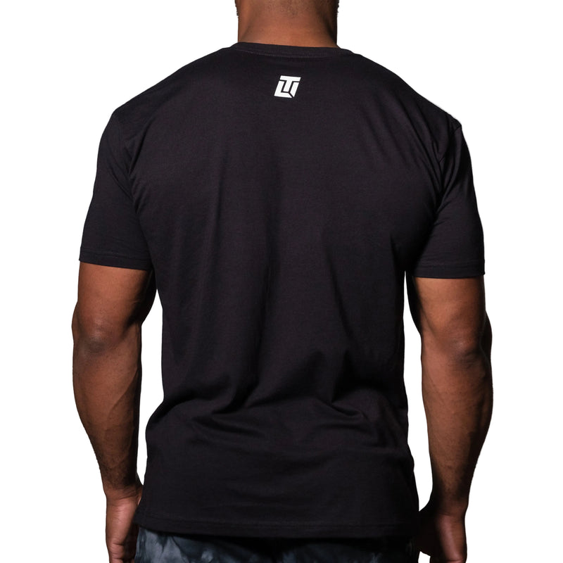 Load image into Gallery viewer, Black t-shirt with a logo on the back worn by a person against a gray background
