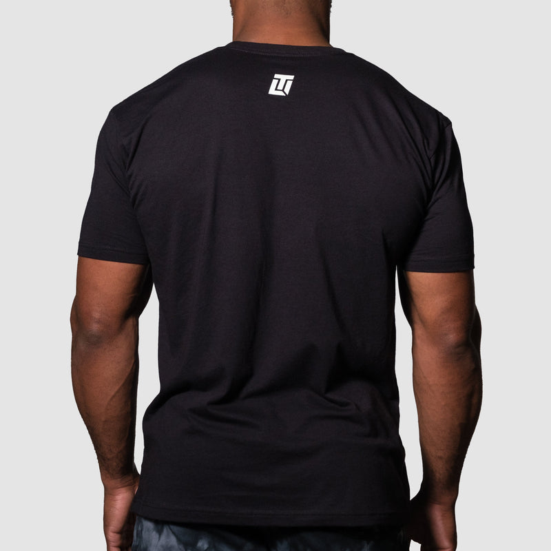 Load image into Gallery viewer, Black t-shirt with a logo on the back worn by a person against a gray background
