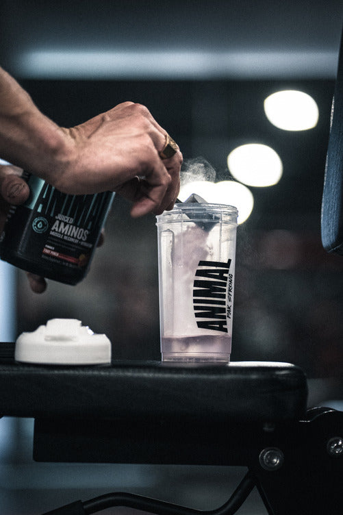 Load image into Gallery viewer, image of a hand pouring a scoop of Animal Juiced Aminos in a cup of water.